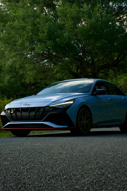 a blue car is parked in the shade by some trees