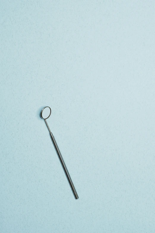 a small long metal rod with a hole to the bottom is against a pale blue backdrop