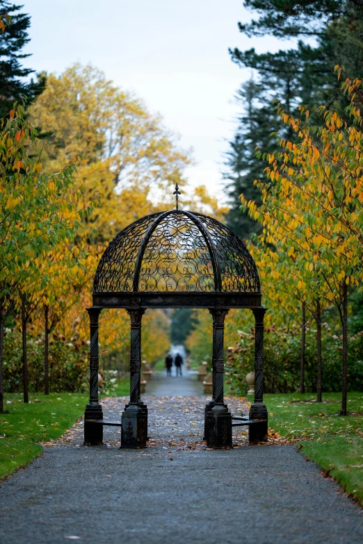 an outdoor gazebo in the middle of a park path with trees that have yellow leaves