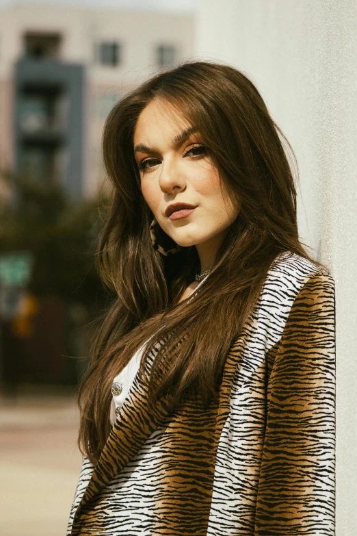 a woman leaning on a wall wearing a black and brown jacket