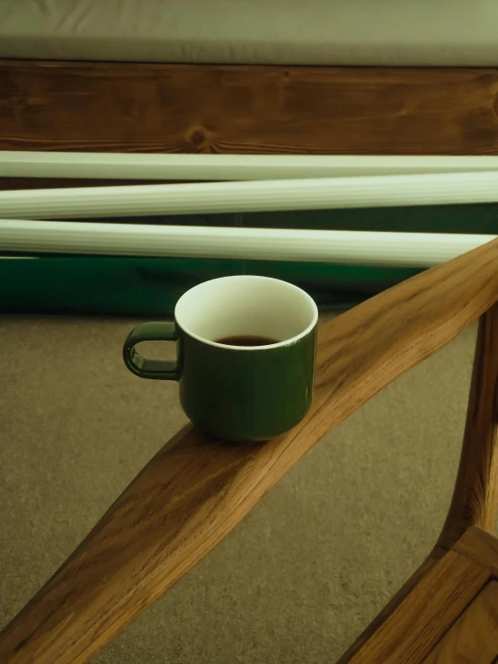 a green cup of coffee sits on a wooden bench