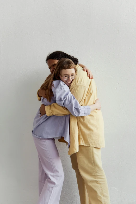 two people hugging each other, with a wall in the background