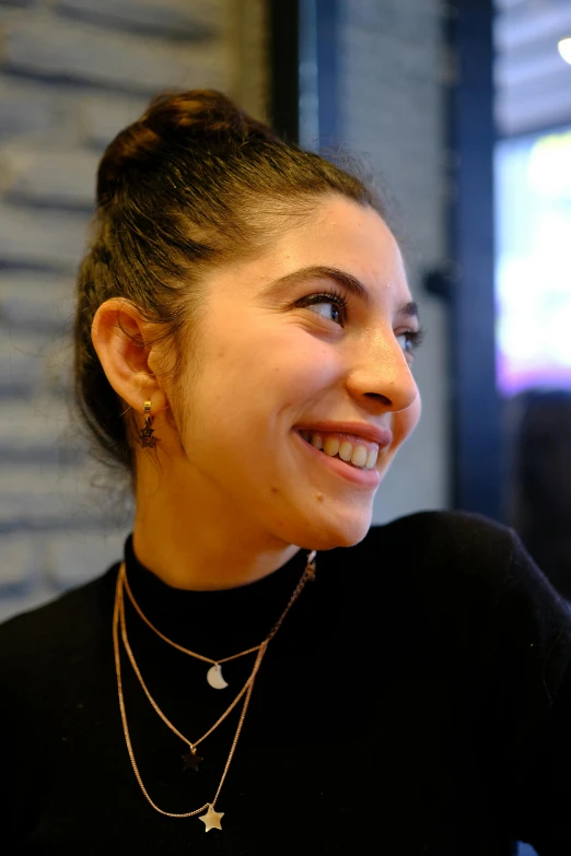 a young woman smiling wearing a necklace and standing in front of a gray brick wall