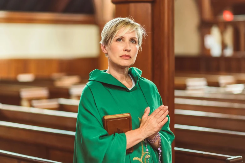 a woman in a green jacket holding her hands together in a pew