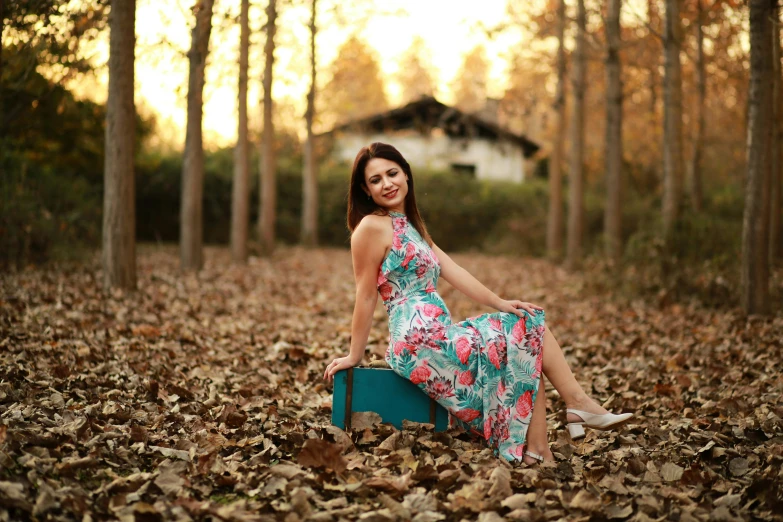 an attractive young woman sitting on a suitcase in a park