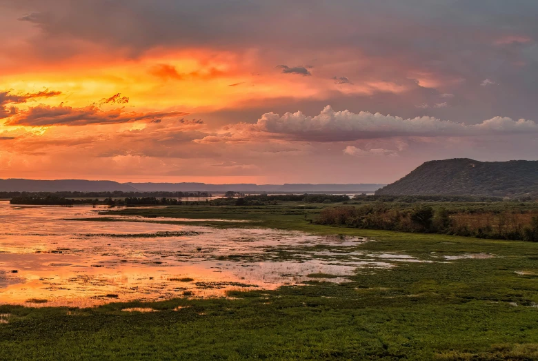 a body of water surrounded by grass and a hill