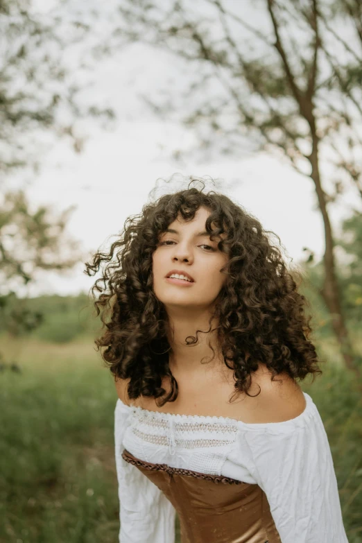 a woman with curly hair standing in front of trees