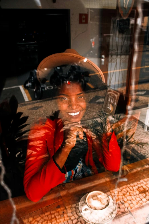 a woman with a hat smiles through a shop window