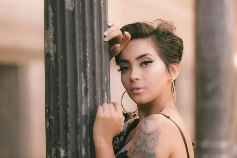 an asian woman wearing large hoop earrings leaning against a pillar