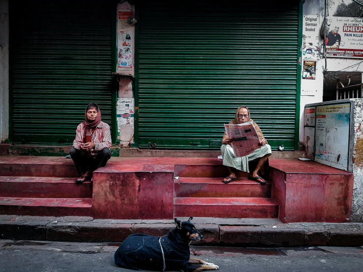 two people sitting on stairs next to a dog on the street