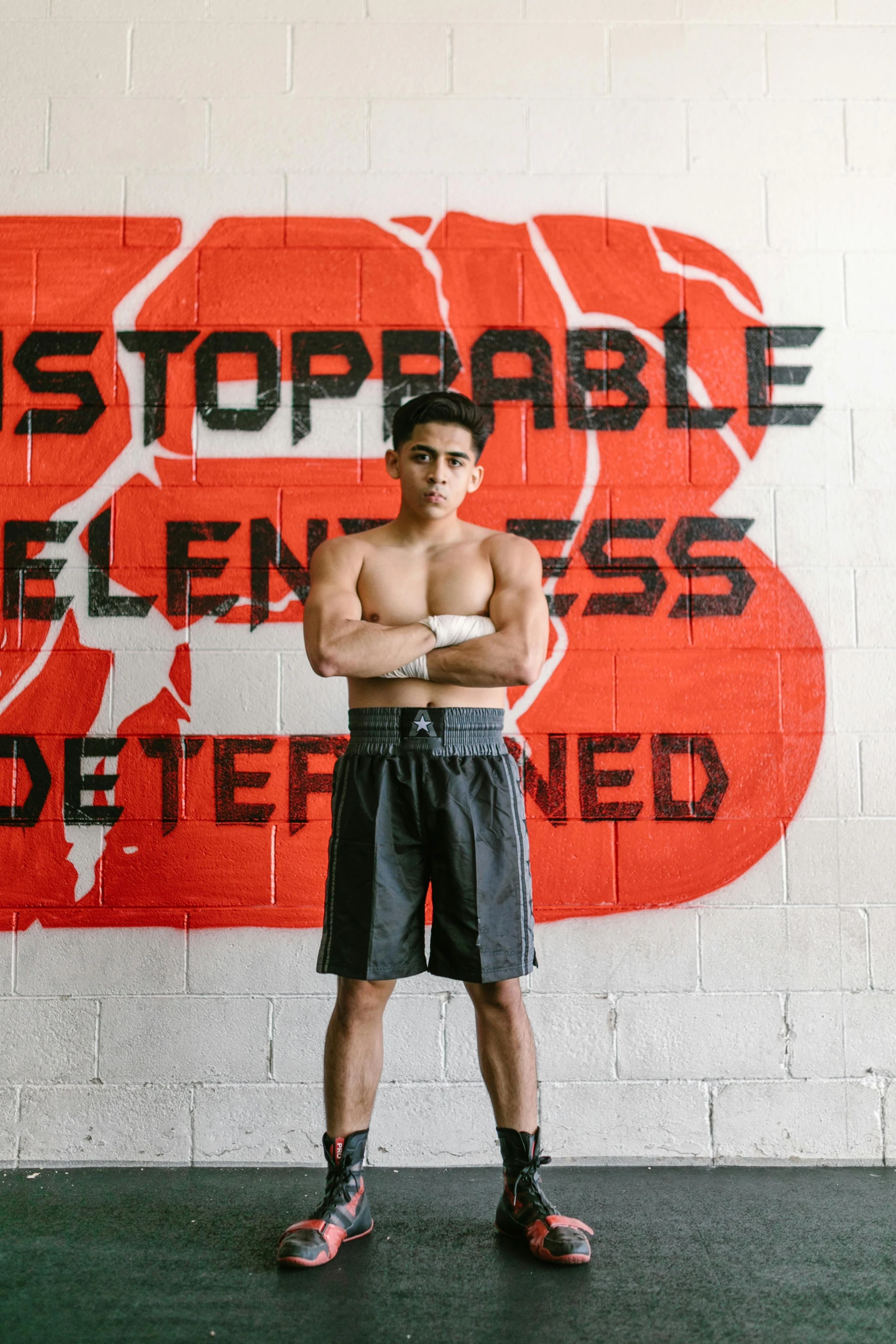 young man posing with arms crossed against wall with words on it