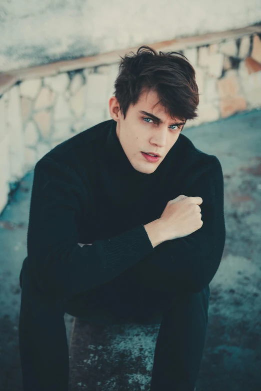 a young man poses while wearing black sweater