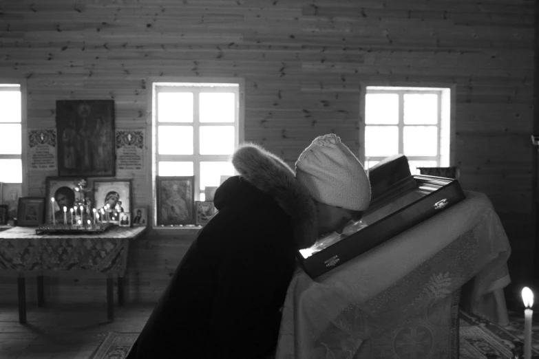 black and white pograph of woman with long hair and hat in living room with books and candles