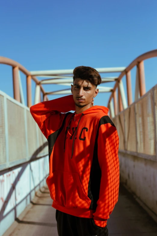 a young man standing on a bridge, wearing an orange and black jacket