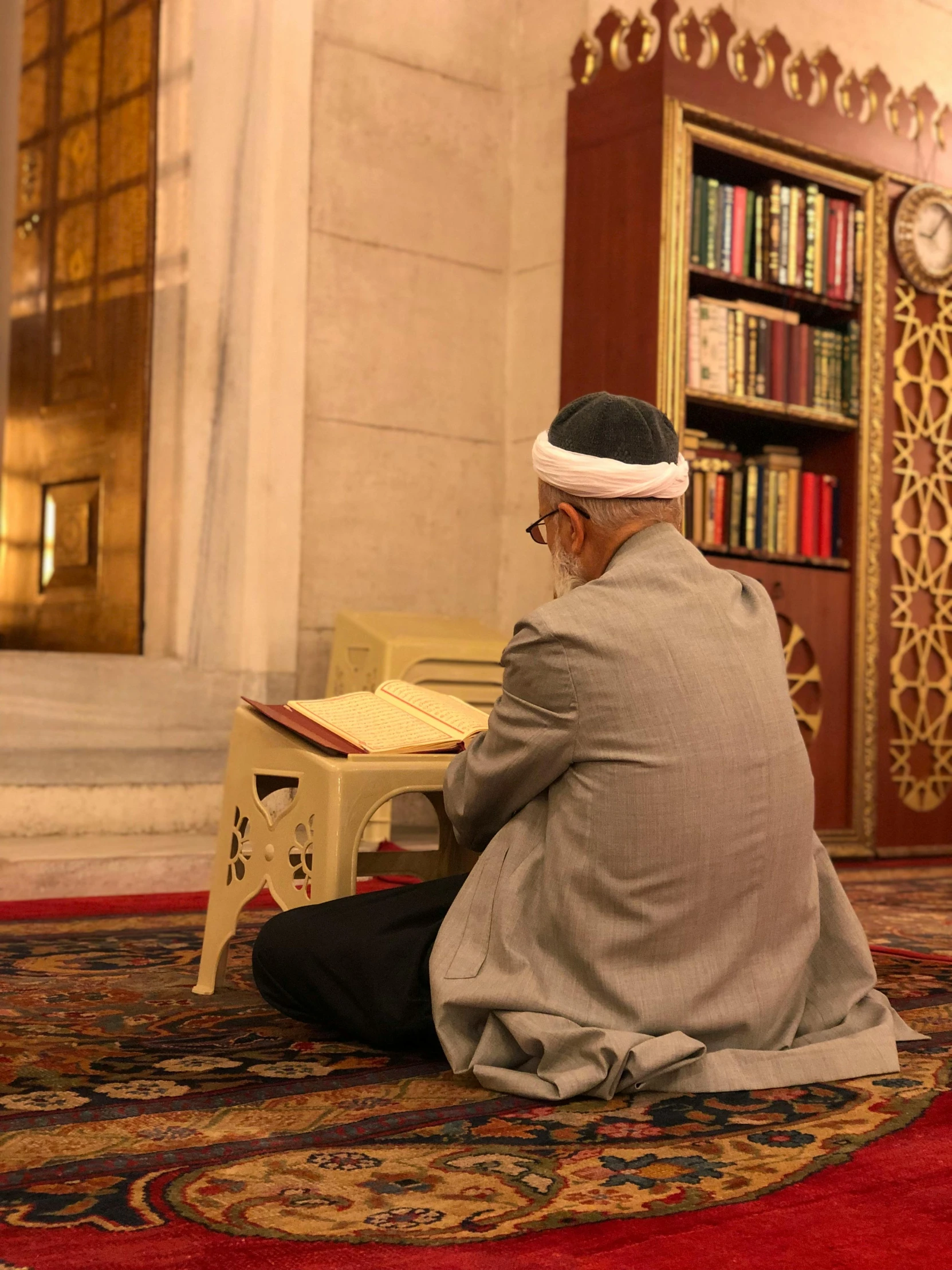 a man kneeling down reading a book while sitting on a rug