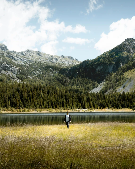 a man standing by a lake on the side of a mountain