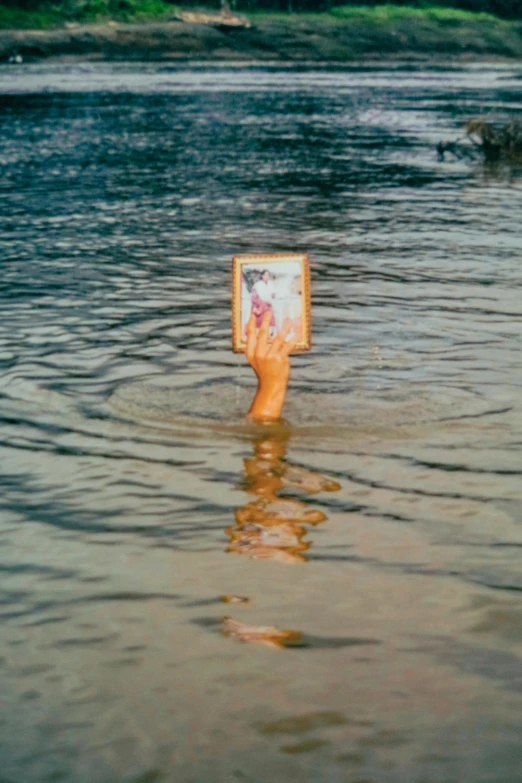 someone holds up a picture while standing in the middle of water