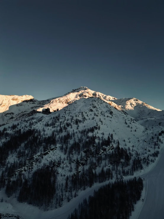 a mountain top with snow covered trees and a few clouds in the sky