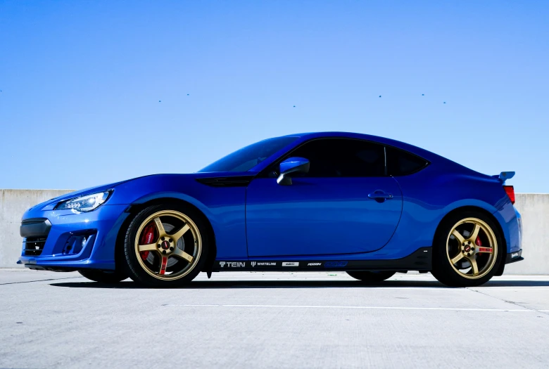 the blue sports car with gold rims sits in an empty lot