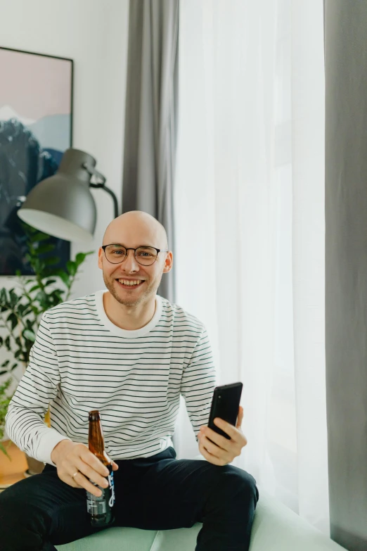 a man sitting on a couch holding a beer and looking at his cellphone