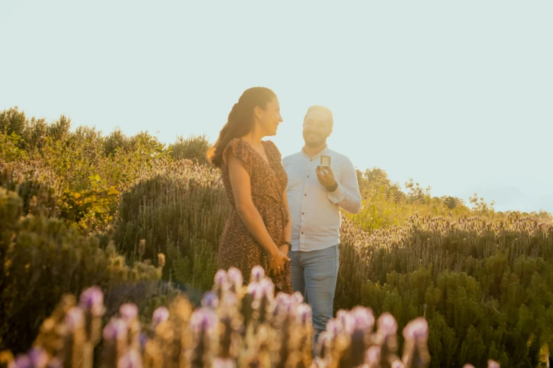 a man and woman in grassy field next to purple flowers