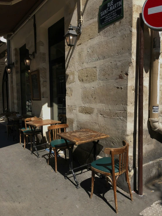 several wooden tables and chairs sit outside of a storefront