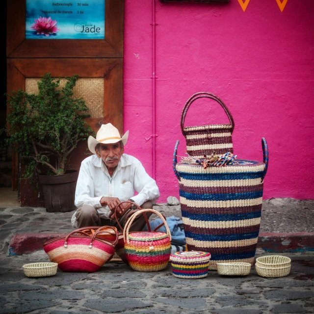 a man sitting on the ground next to several bags and baskets