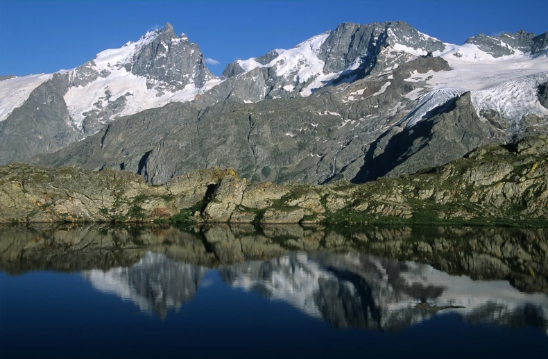 some snow capped mountains reflecting in the still water of a lake