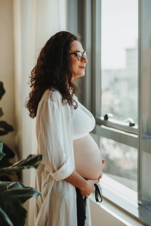 a pregnant woman standing by a window looking at her belly