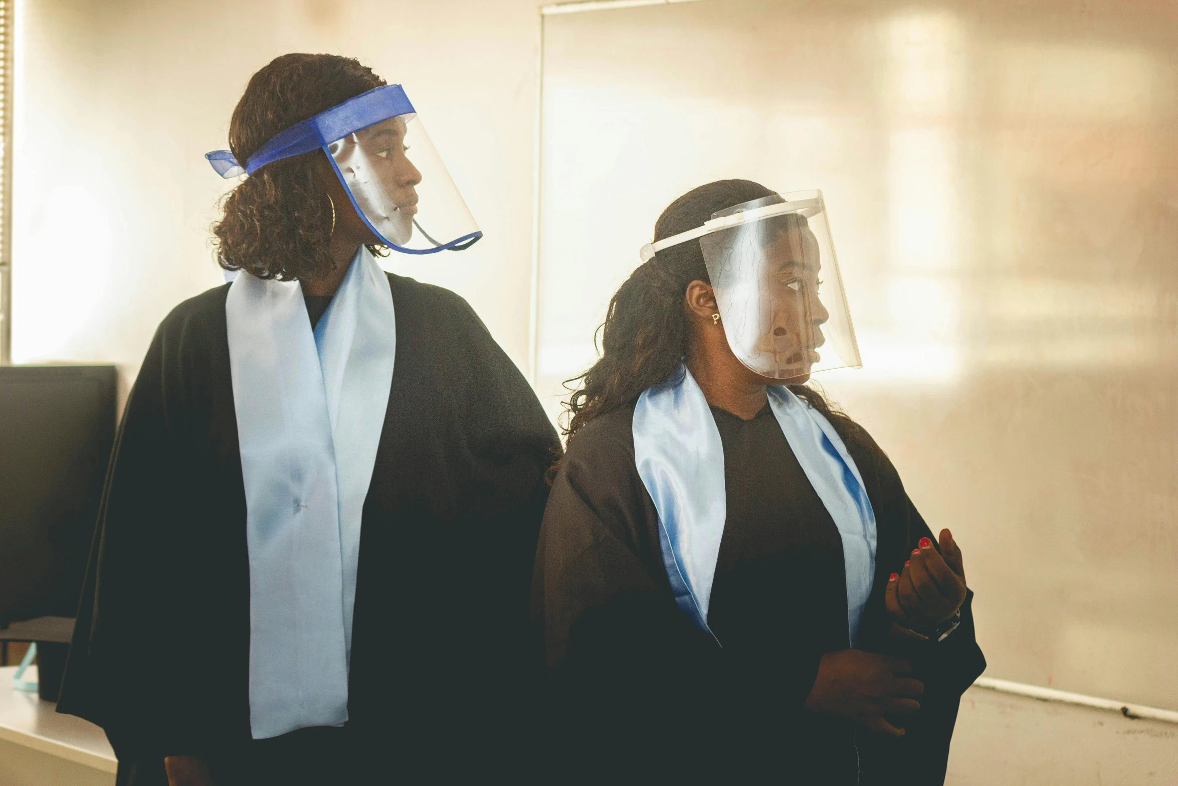 two women are wearing protective visors in an office cubicle