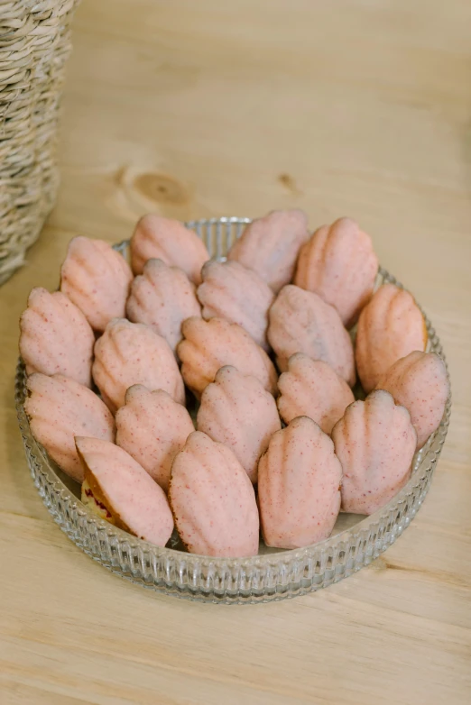 a glass dish of pink donuts next to a basket of other doughnuts