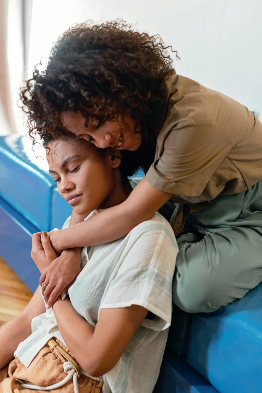 two women sitting on a couch one with her arms around the other