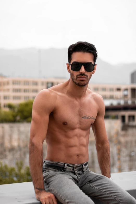 a shirtless man wearing sunglasses and looking at the camera