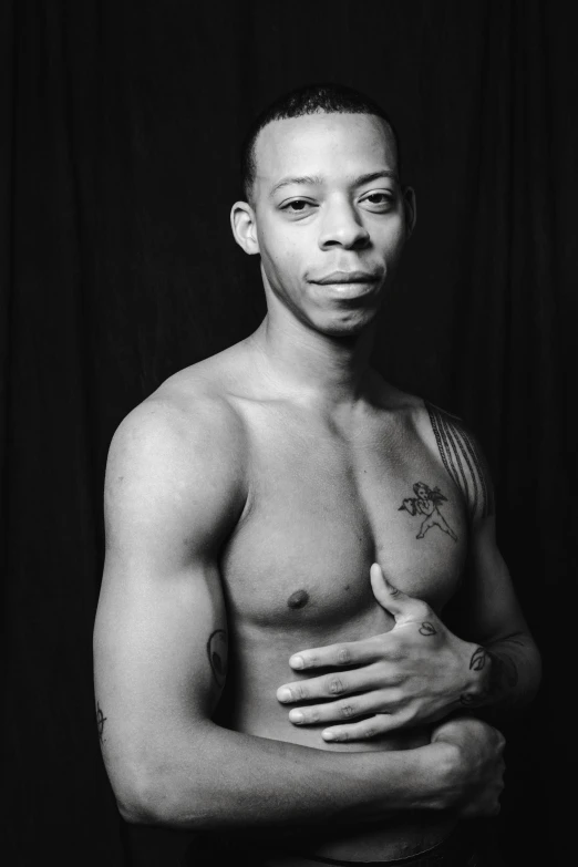 a shirtless man standing against a black backdrop