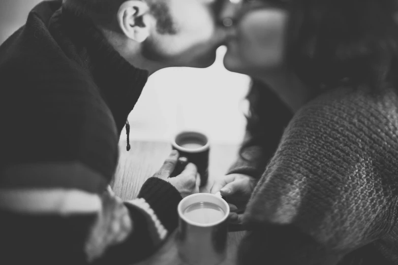 a couple kissing while drinking coffee in a coffee shop