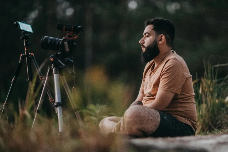 a bearded man sitting with a video camera by himself