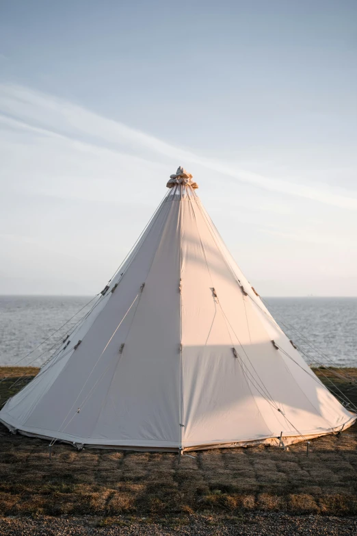 a white tent with ropes and rocks next to the ocean