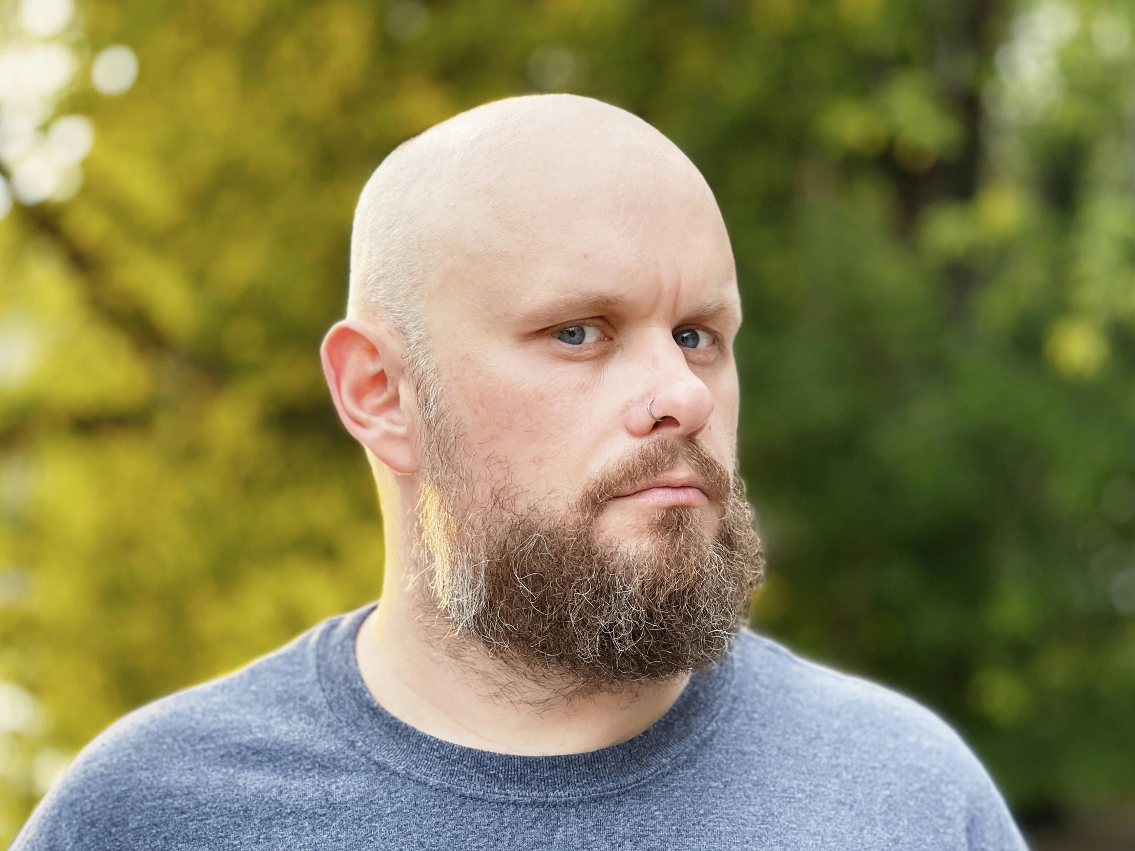 a man with shaved hair and beard wearing blue t - shirt