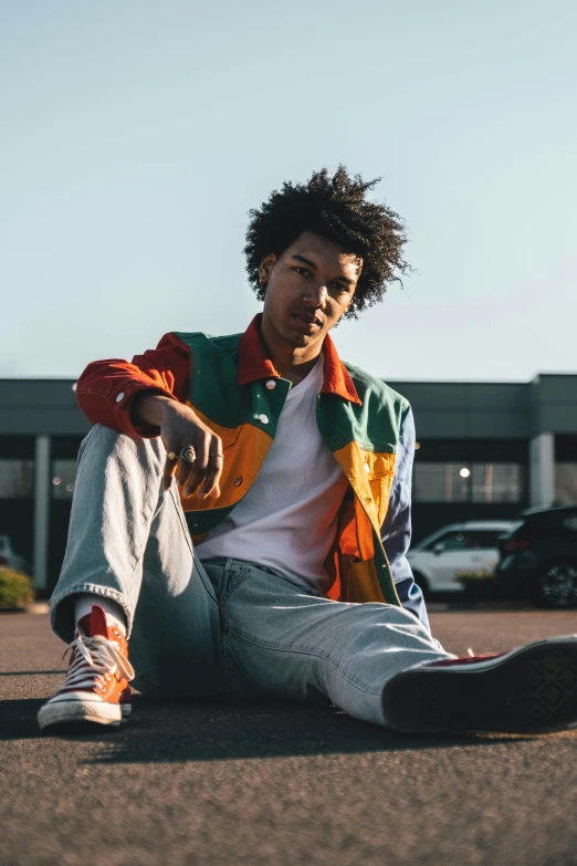 a young man sitting on the ground in front of cars