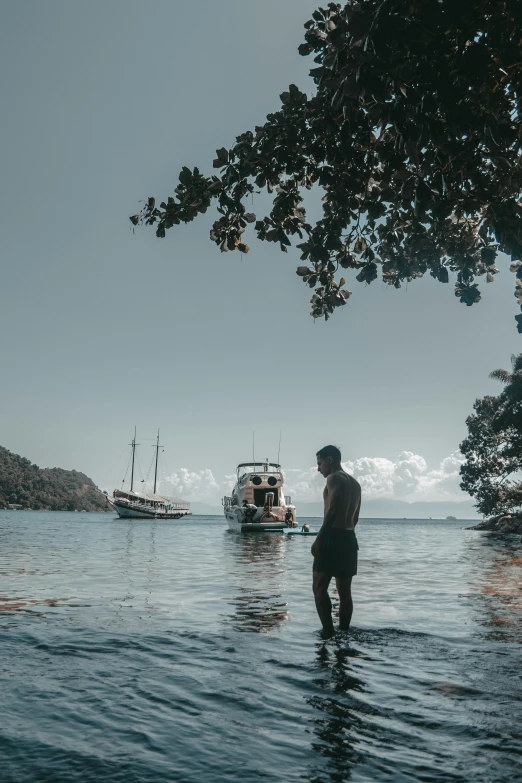 a man standing in the water watching a boat pass