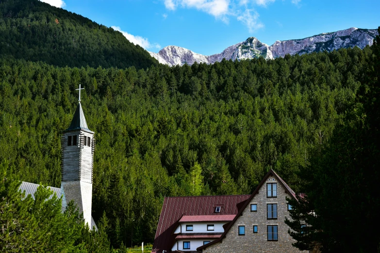 a church building stands on a hilltop next to some forest