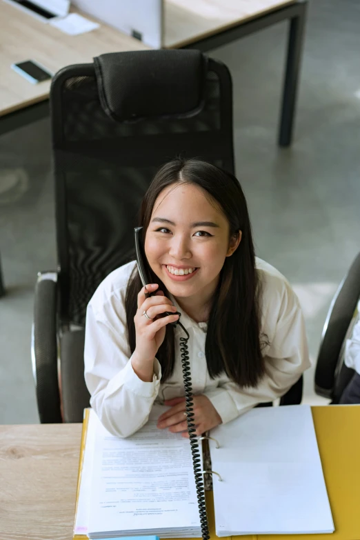 a girl talking on a telephone while sitting at her desk