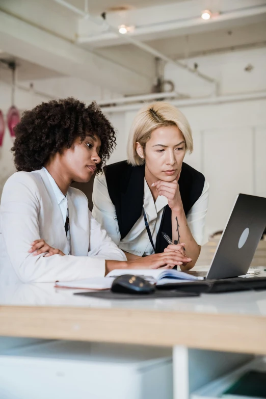 two women look at a computer screen while seated down