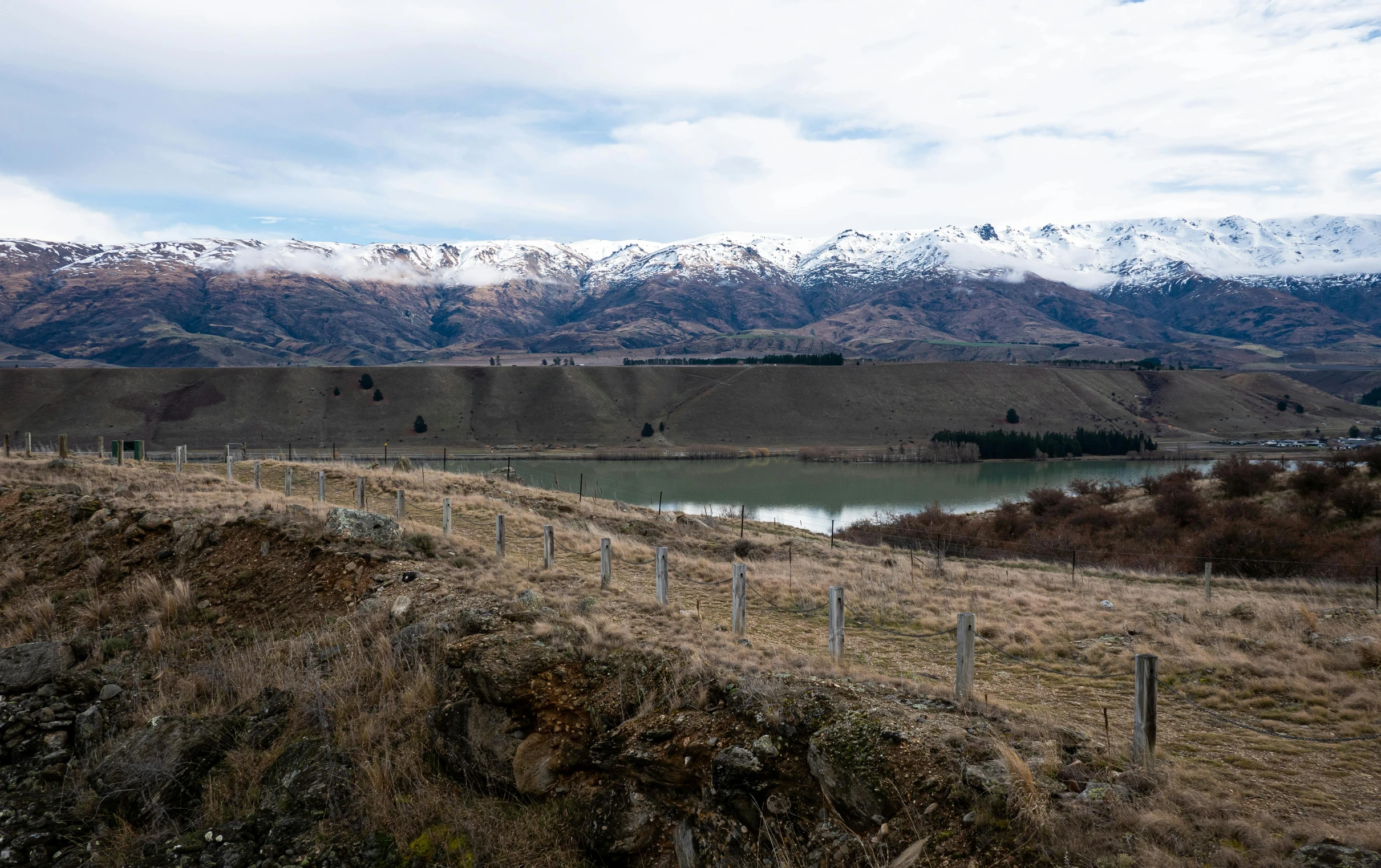 a landscape with mountains, a body of water and a fence