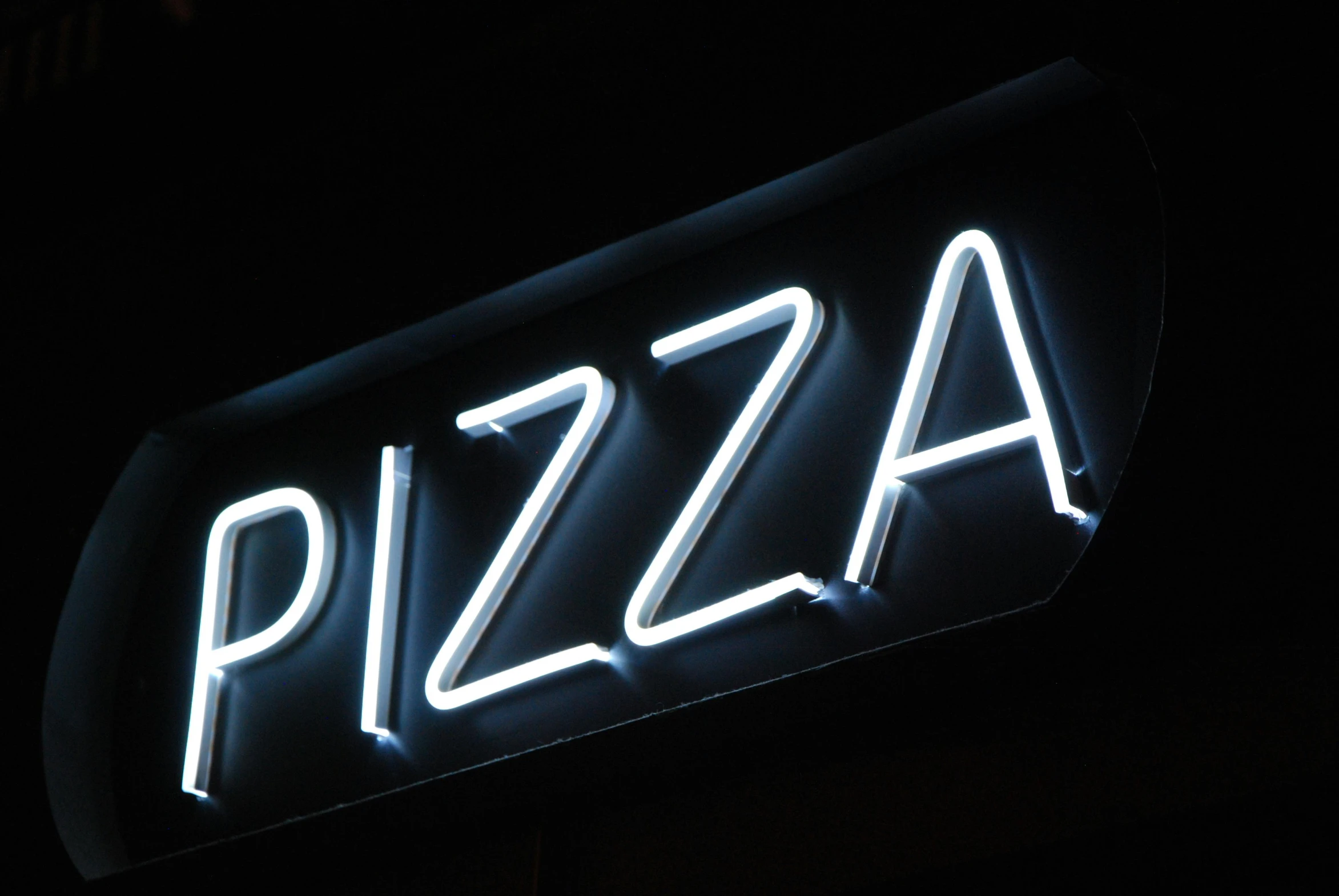 the neon sign reads pizza in white letters