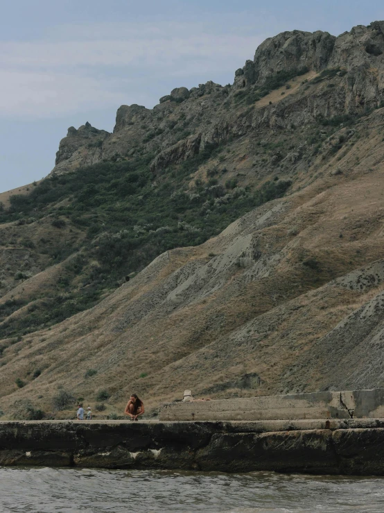 a person sitting on the rocks overlooking water next to mountains