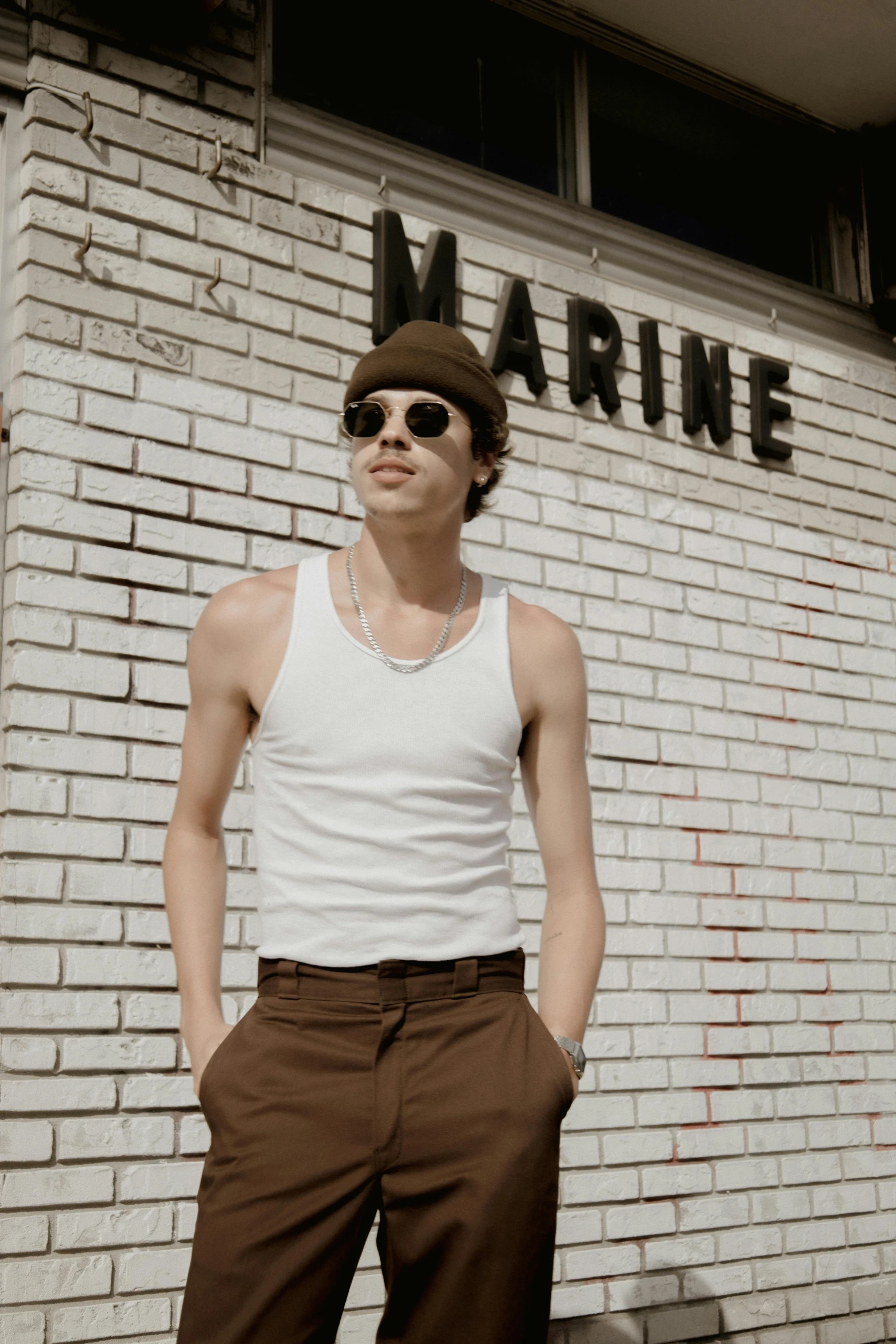 man wearing sunglasses stands in front of a brick wall