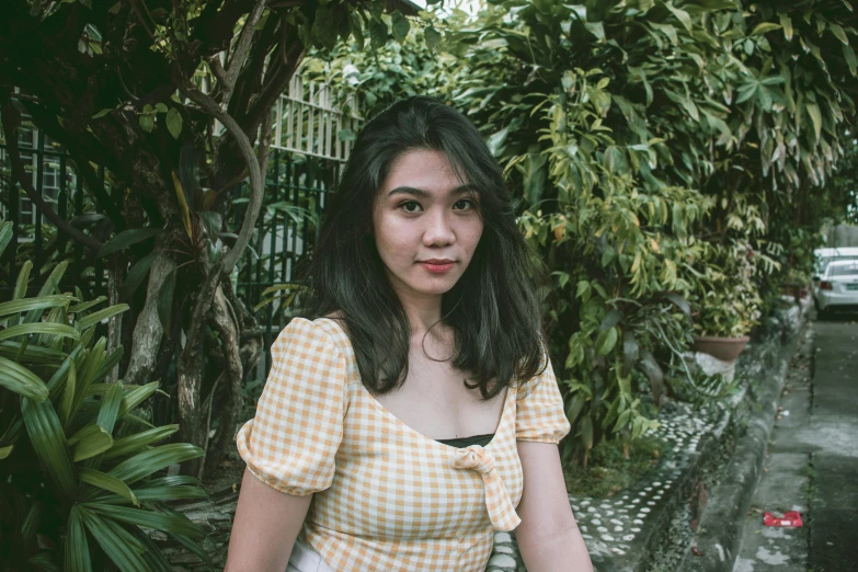 a girl with a collar dress posing on a bench in the middle of some trees