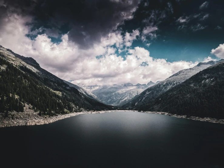 a lake surrounded by a mountain range under a cloudy sky