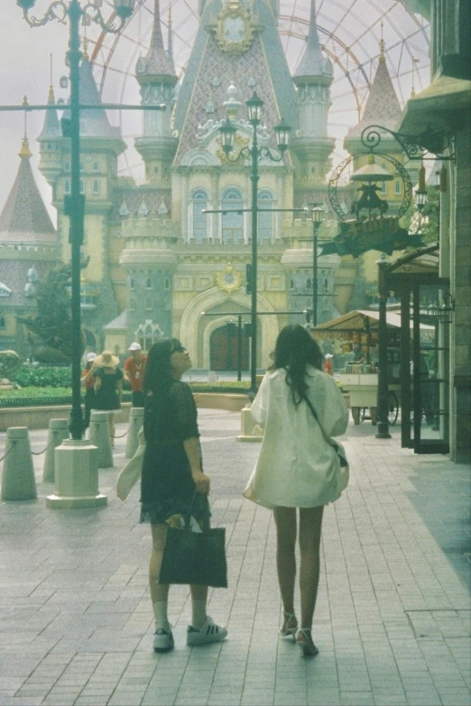 two women are standing on the side walk, waiting for soing